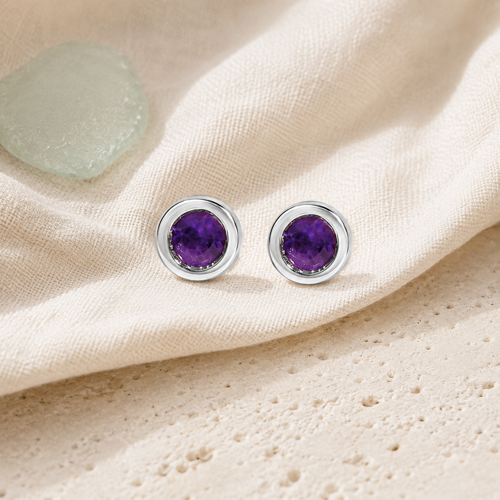 Purple amethyst stud earrings styled on ivory linen and pale stone