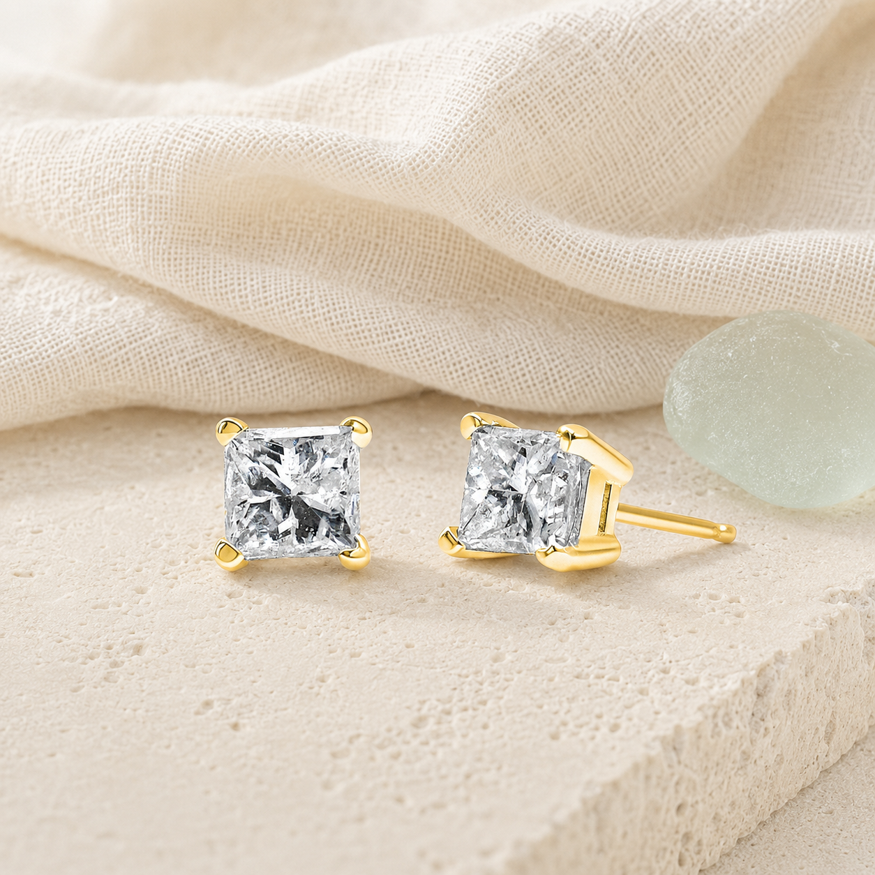 Princess-cut diamond stud earrings styled on ivory linen and limestone