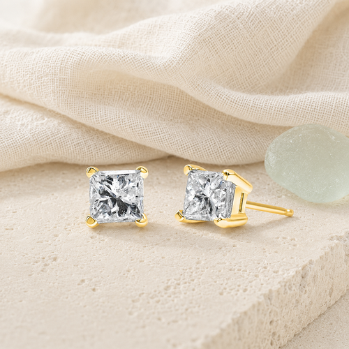 Princess-cut diamond stud earrings styled on ivory linen and limestone
