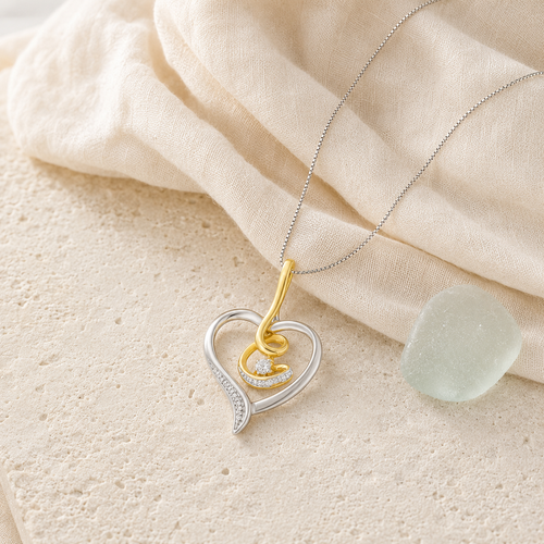 Two-tone gold diamond swirl heart necklace styled on ivory linen and sea glass